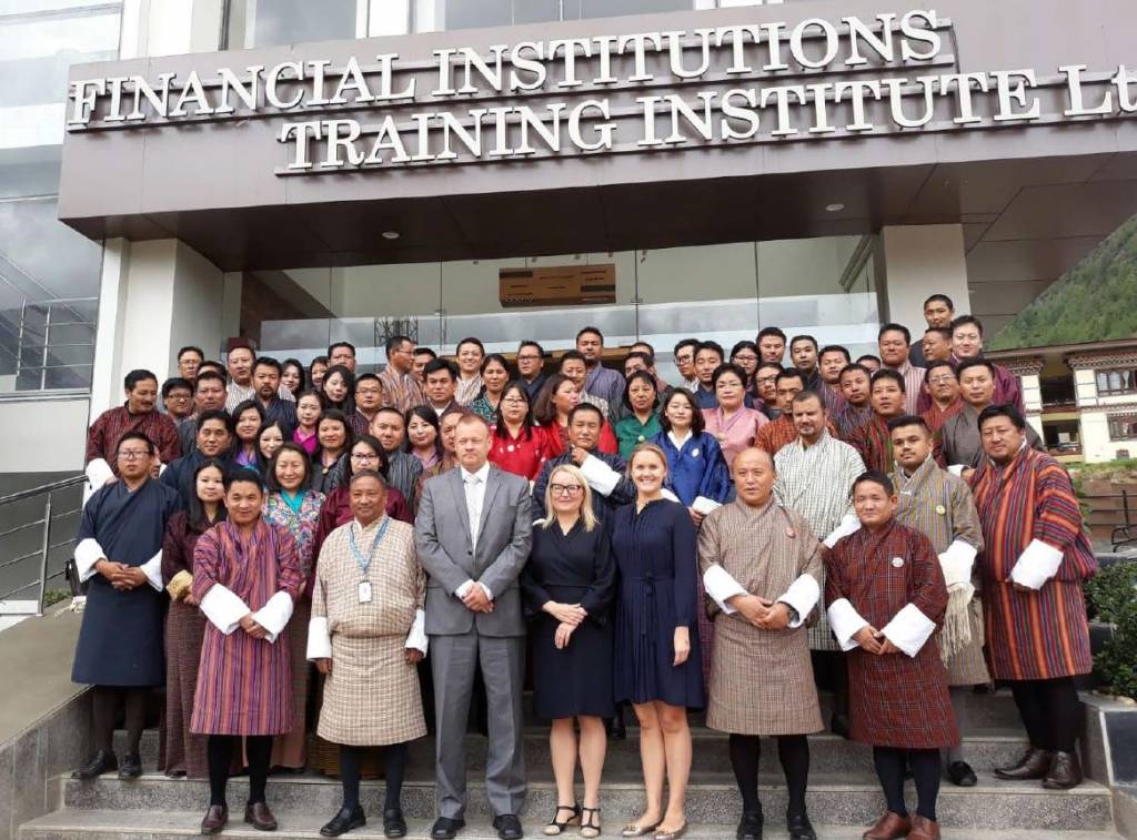 A group of people posing for a photo in front of a building entrance. The text ‘Financial institutions training institute’ is written above the entrance. Photo.